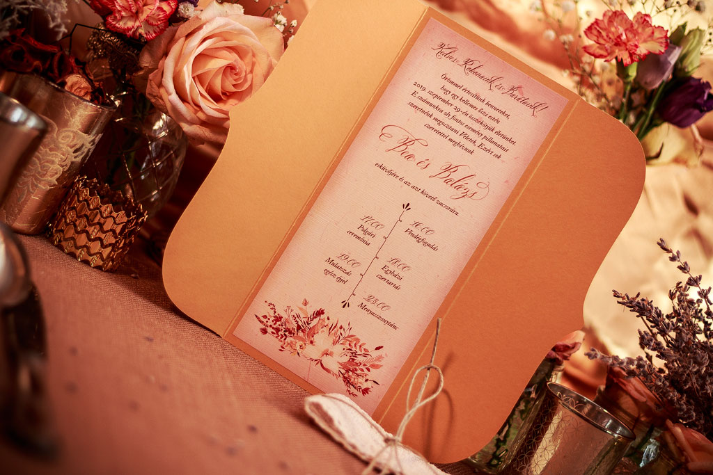 Csipkés esküvői meghívó őszi színekben pompázó, ívelt formájú tasak, csipkepántos díszítés masnival, kézzel festett virágos grafikák és látványos tipográfia