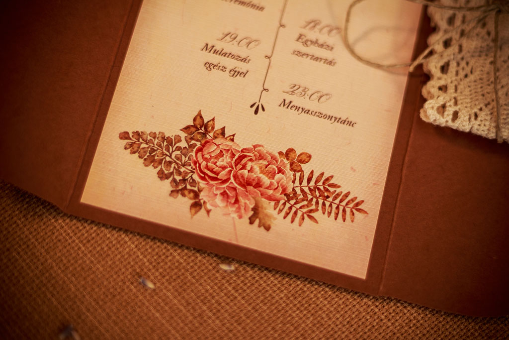 Csipkés esküvői meghívó őszi színekben pompázó, ívelt formájú tasak, csipkepántos díszítés masnival, kézzel festett virágos grafikák és látványos tipográfia