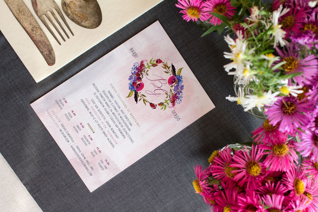 Bohó és kékvirágos esküvői meghívó élénk bordó és pink árnyalatokkal, lila, bogyósgyümölcs grafikával, tollakkal és rusztikus kalligrafikus név kiemeléssel