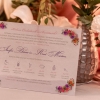 Mezeivirágos bíbor esküvői meghívó kellemes lila, piros és narancs virágokkal, halvány alnyomattal, modern és elegáns betűtípussal