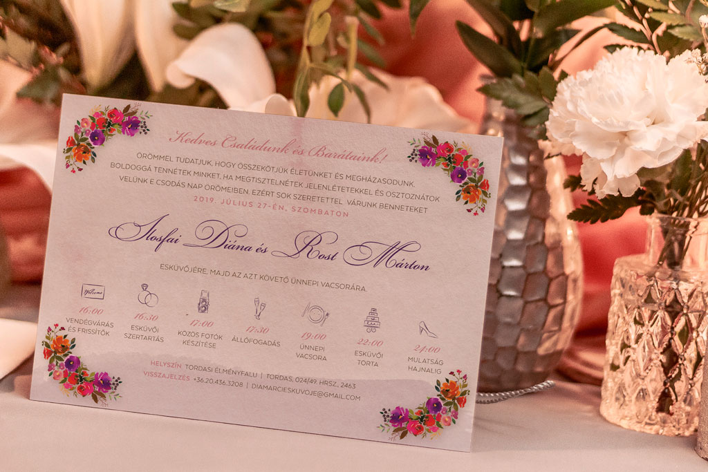 Mezeivirágos bíbor esküvői meghívó kellemes lila, piros és narancs virágokkal, halvány alnyomattal, modern és elegáns betűtípussal 