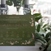 Virágos erdei esküvői meghívó rengeteg zöld levéllel, apró erdei virágokkal pasztel rózsaszín és krém színben, rusztikus hangulatú névkiemeléssel.