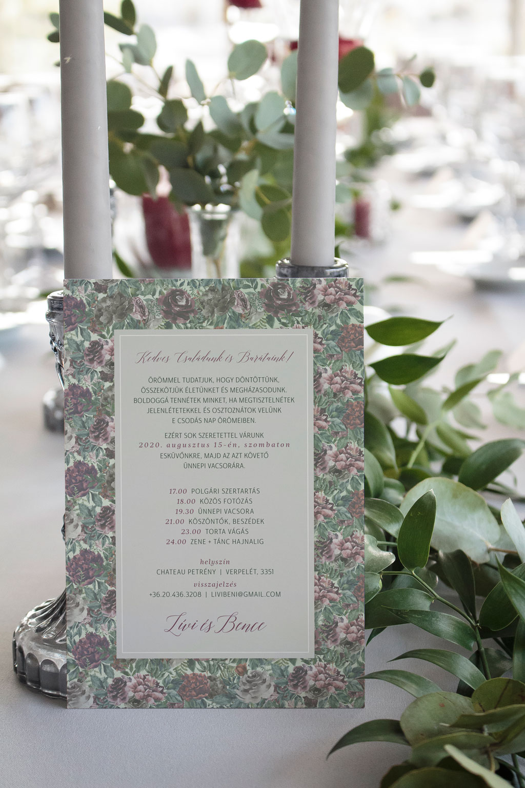 Virágos páfrányos erdei esküvői meghívó rengeteg zöld növénnyel, elegáns sötétlila és bordó virágokkal, halvány zöld alnyomattal és modern tipográfiával.