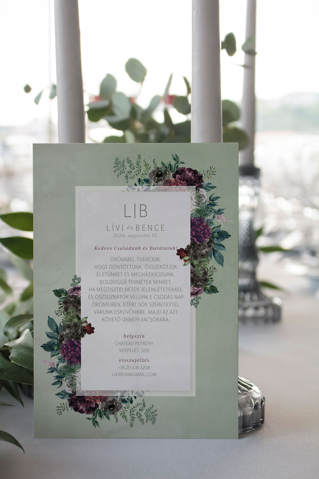 Virágos páfrányos erdei esküvői meghívó rengeteg zöld növénnyel, elegáns sötétlila és bordó virágokkal, halvány zöld alnyomattal és modern tipográfiával.