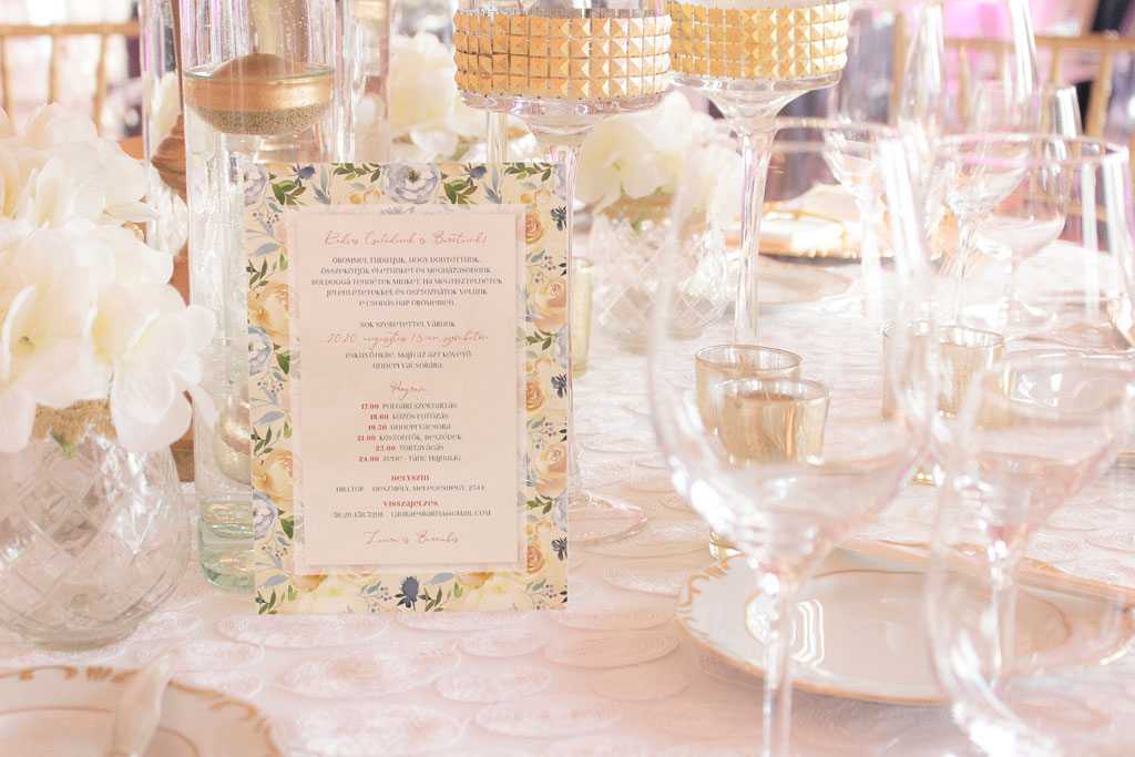 Krém sárga virágos esküvői meghívó, pasztel zöld és szürkéskék levelekkel, meleg sárga árnyalatú, márványos alnyomat grafikával és elegáns tipográfiával. 