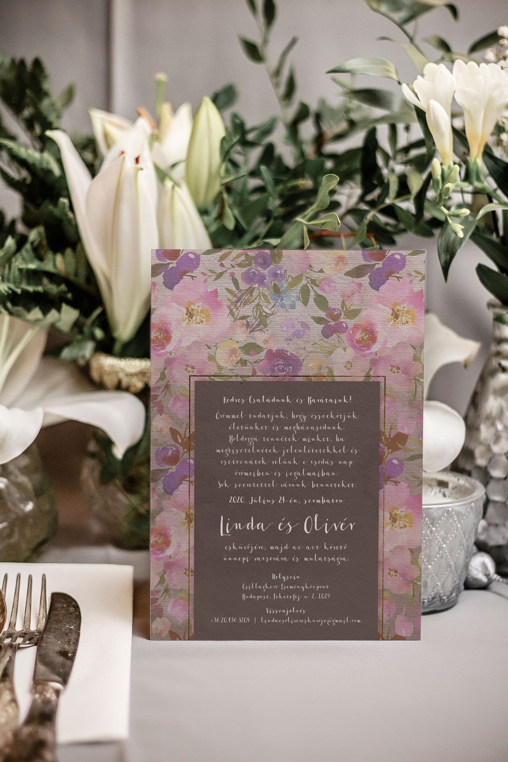 Tavaszi virágos esküvői meghívó halvány rózsaszín, élénk pink és ciklámen, apró kék és krém virágos, zöld leveles grafikával, drapp alnyomattal.