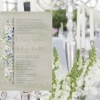 Téli virágos esküvői meghívó halvány szürkéskék apró virágokkal. Lila bogyós növénnyel és zöld levéllel. Zöldes szürke vízfestékes alnyomat grafikával.