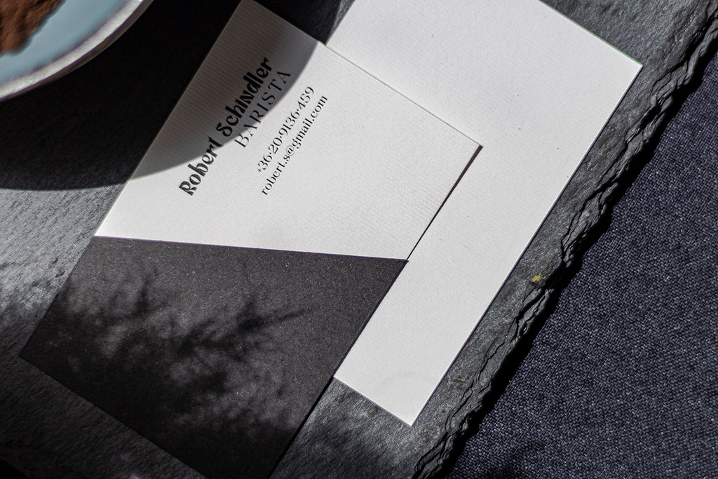 Fekete-fehér névjegy kétféle papírból különböző felületű textúrákkal kézzel ragasztva, színes hátoldallal kérhető prémium változatban is