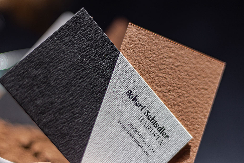 Fekete-fehér névjegy kétféle papírból különböző felületű textúrákkal kézzel ragasztva, színes hátoldallal kérhető prémium változatban is