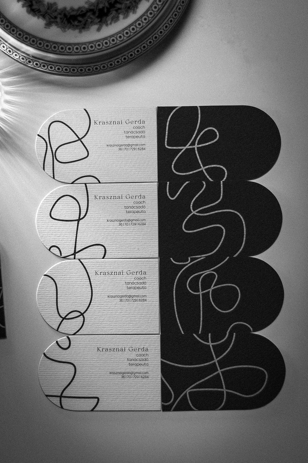 Háromrétegű boltíves névjegy digitfehérrel fekete-fehér-piros színkombinációban, mindkét oldalán nyomtatva 25 féle grafikai motívummal egyedi formára vágva