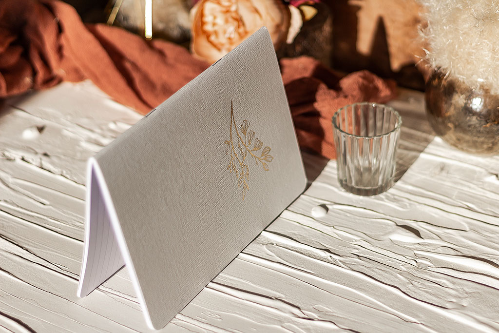 Szürke vászonfelületű füzet arany virággal prégelve: A/5, 64 oldalas, pontozott vonalas, fehér belívvel, sarokkerekített, egyedi paraméterekkel is rendelhető