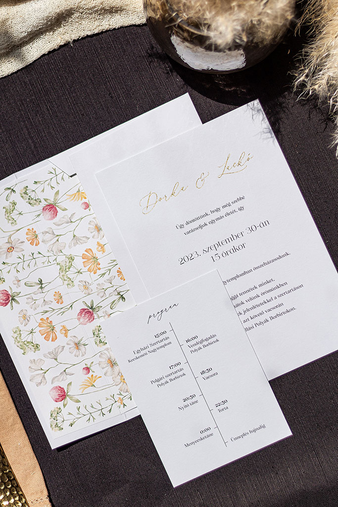 Egyedi névaranyozással díszített esküvői meghívó és boríték, virágos grafikával nyomtatott ragasztott béléses borítékkal és program kártyával