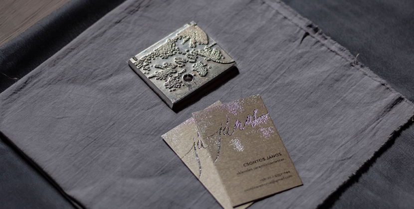 Textúrált prégeléssel díszített névjegykártya ezüstösen csillogó prémium papíron, fekete szöveg nyomtatással egyedi grafikai tervezéssel
