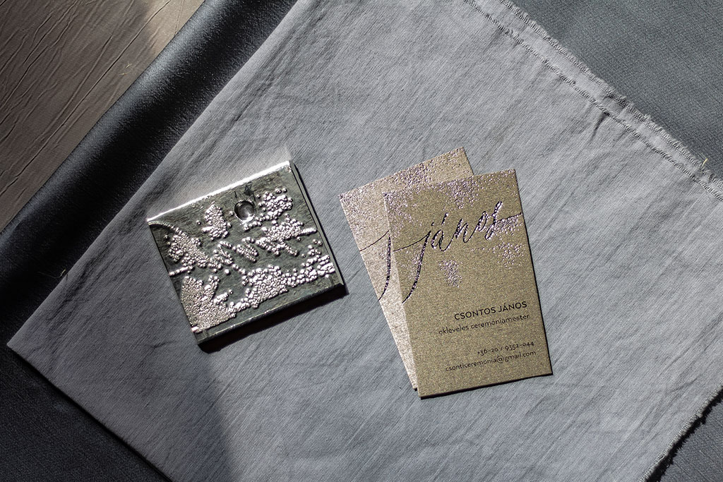 Textúrált prégeléssel díszített névjegykártya ezüstösen csillogó prémium papíron, fekete szöveg nyomtatással egyedi grafikai tervezéssel